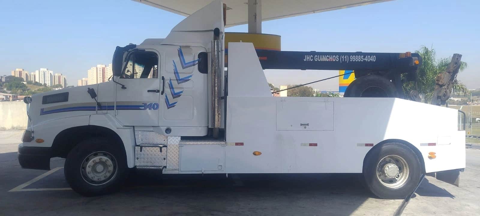 Guincho pesado da JHC visto de perfil, com a lança de reboque recolhida sobre a plataforma.