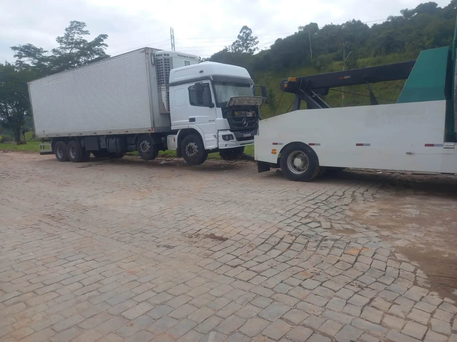 Caminhão baú frigorífico sendo engatado pela lança do guincho pesado da JHC em pátio de paralelepípedo.