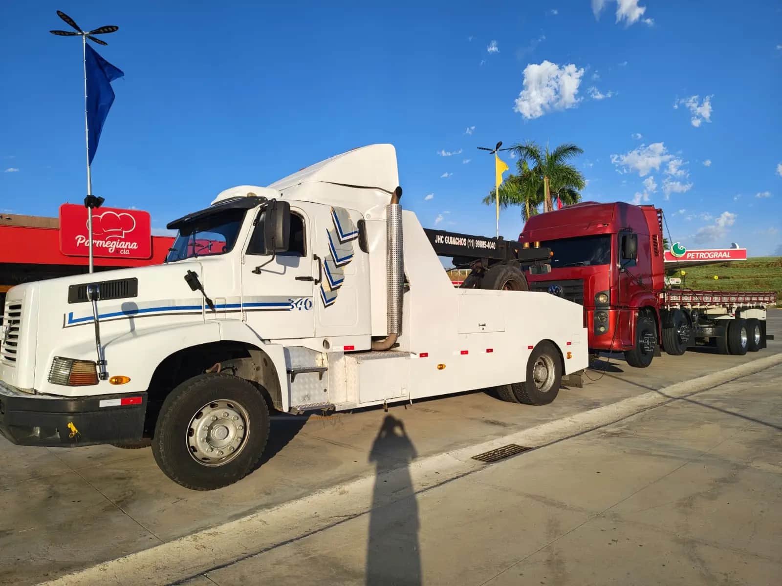 Guincho pesado da JHC de perfil, com um cavalo mecânico vermelho acoplado atrás, no pátio de um posto de estrada.